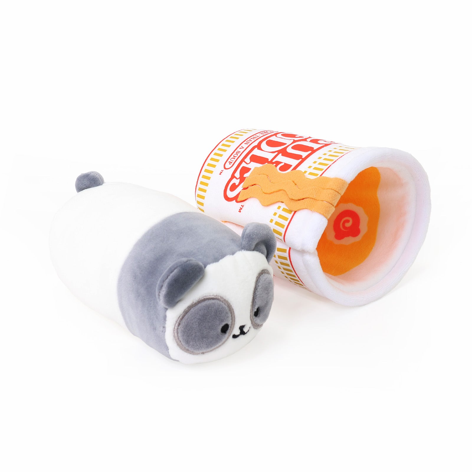 Gray and white panda Pandaroll plush toy lying next to a Cup Noodles-themed plush cup tipped on its side, revealing orange noodle and narutomaki toppings inside, on a white background