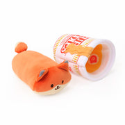 Orange fox Foxiroll plush toy lying next to a Cup Noodles-themed plush cup tipped on its side, revealing orange noodle and narutomaki toppings inside, on a white background